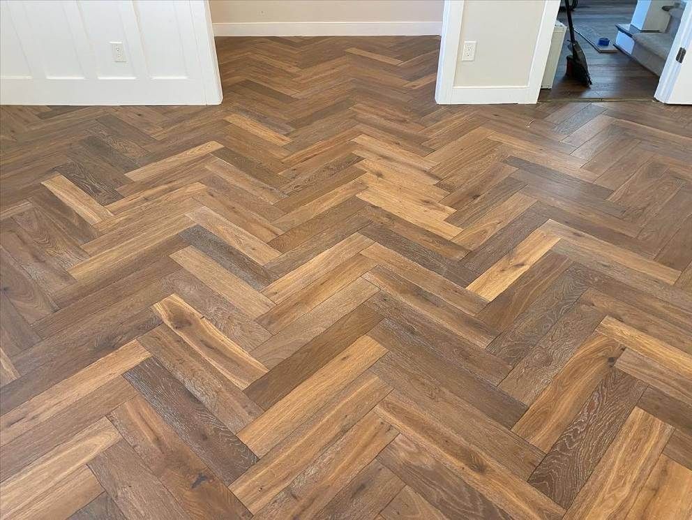 Herringbone wood floor in a room doorway, with medium-brown planks and white walls.