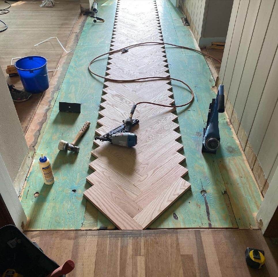 Tools and hose on a long plank floor installation in progress, with blue bucket and wood-pattern panels