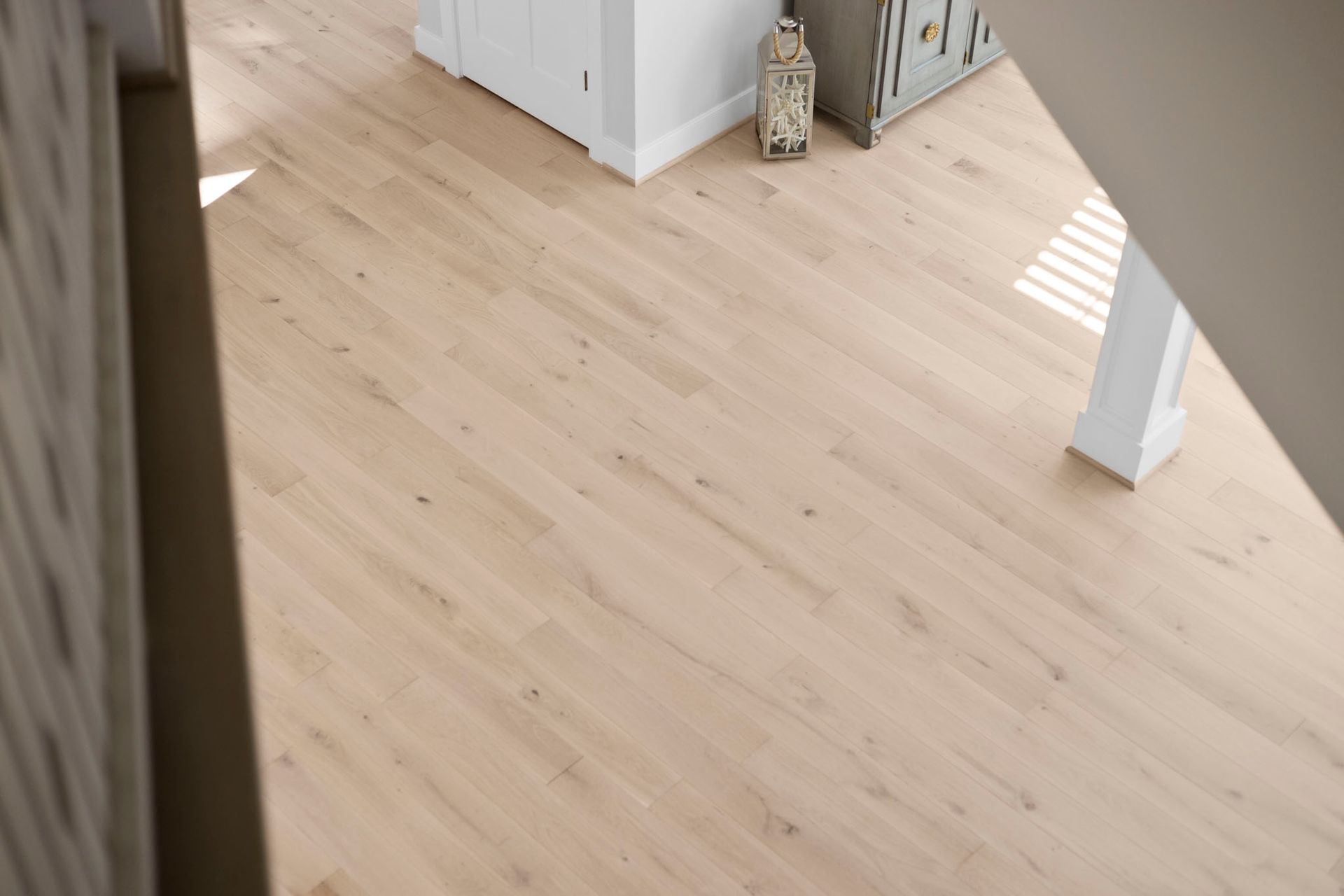 Empty light wood floor in a bright room with a white cabinet and small decor pieces.