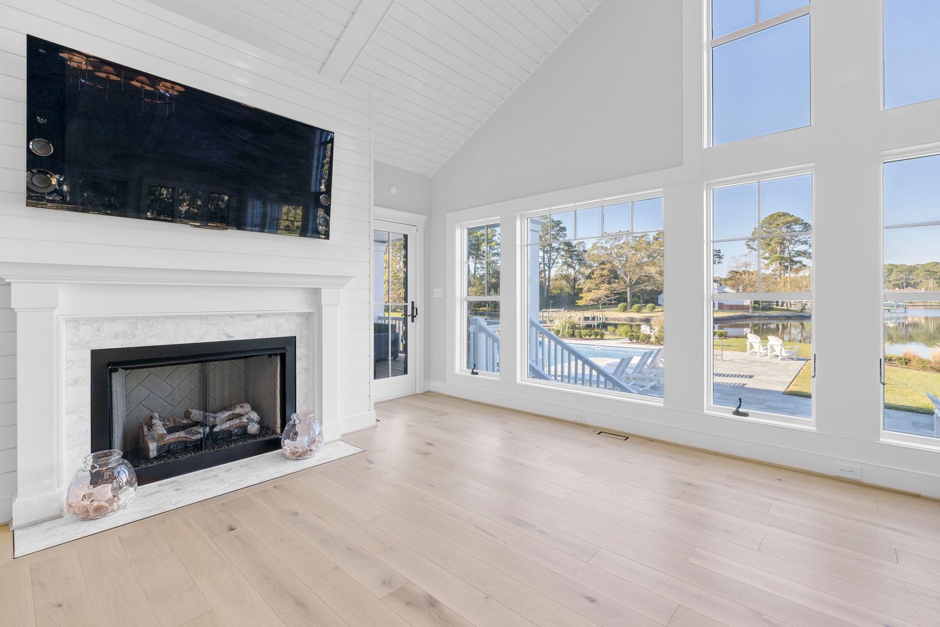 Bright living room with a white fireplace, wall-mounted TV, and large windows overlooking water and trees