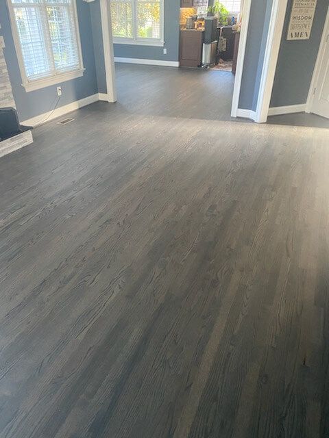 Empty room with gray wood-look flooring and blue-gray walls, lit by daylight from windows.