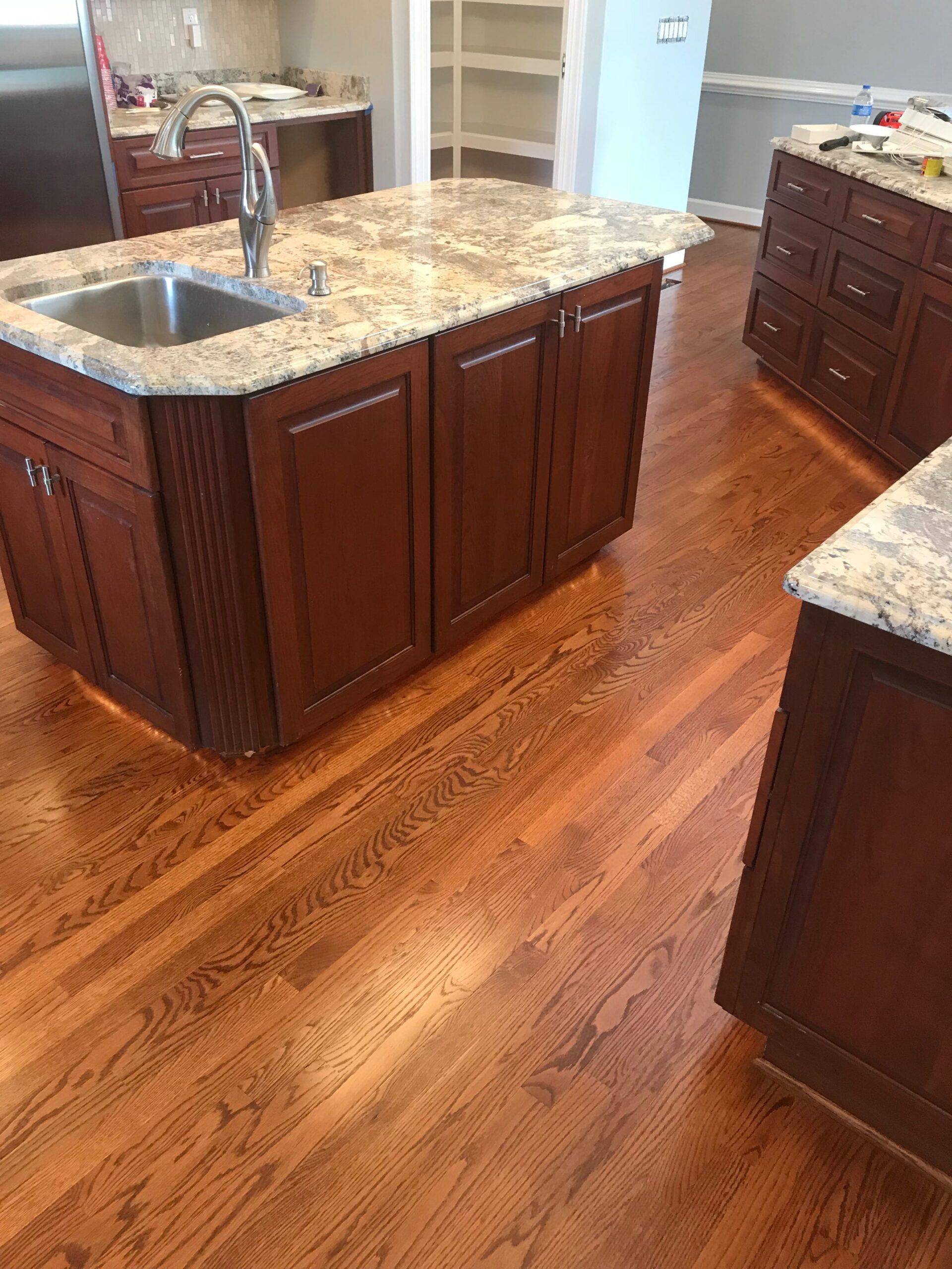 Kitchen with dark wood cabinets, granite island, sink, and hardwood floor.