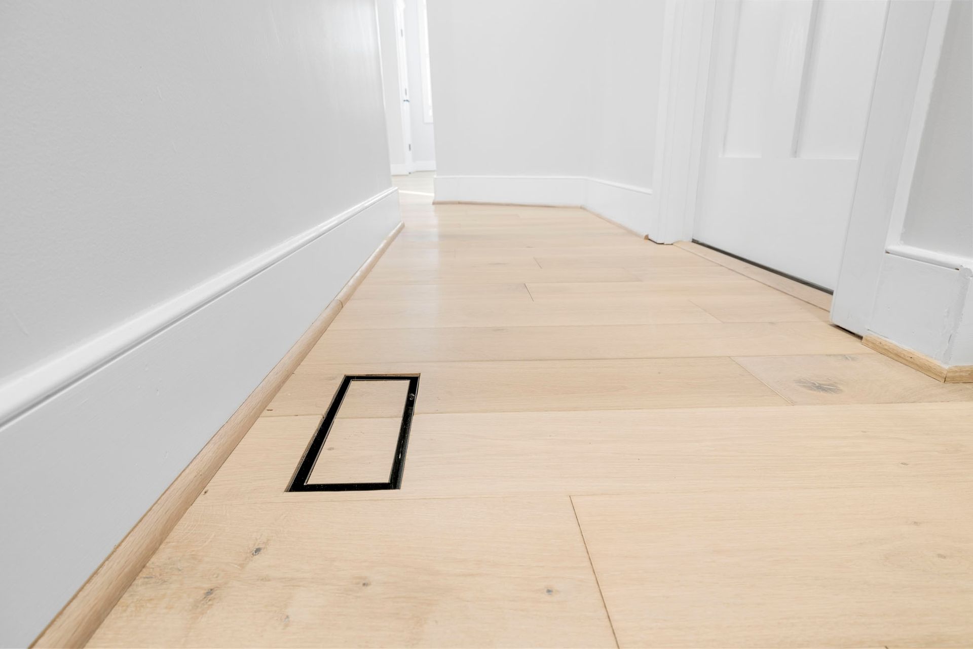 White hallway floor with a black rectangular marker near the baseboard and a closed door on the right