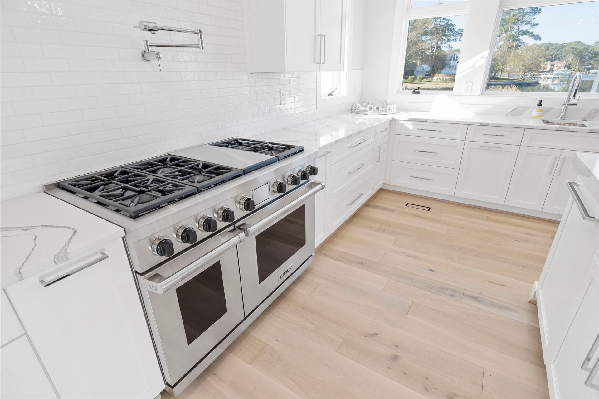 Bright white kitchen with stainless steel stove, white cabinets, and light wood floors.