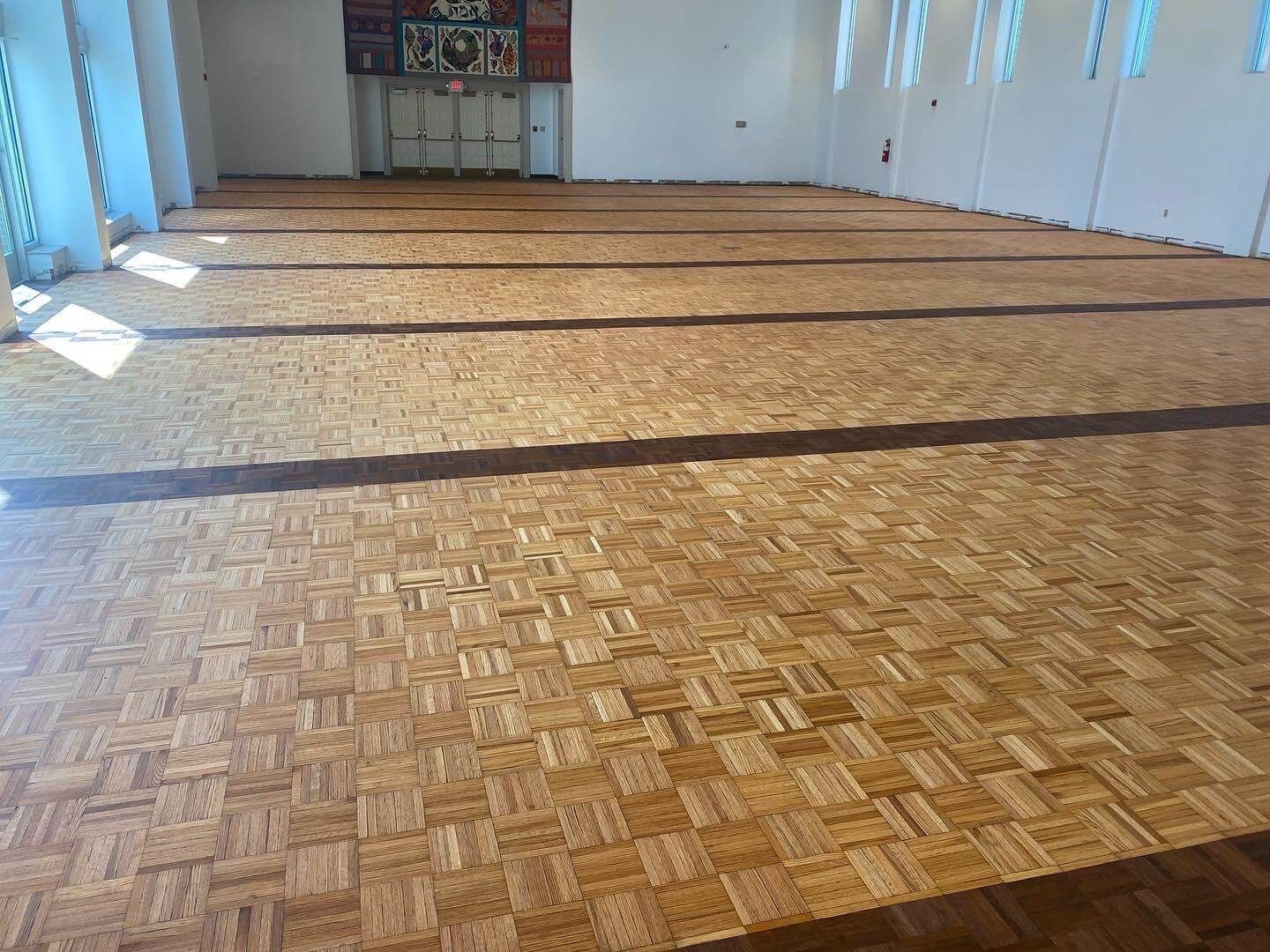 Empty room with a woven wooden floor and windows along the left wall.
