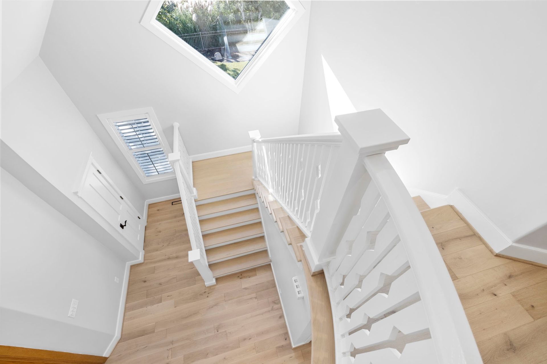 Bright white stairwell with wooden steps and railing under a skylight.