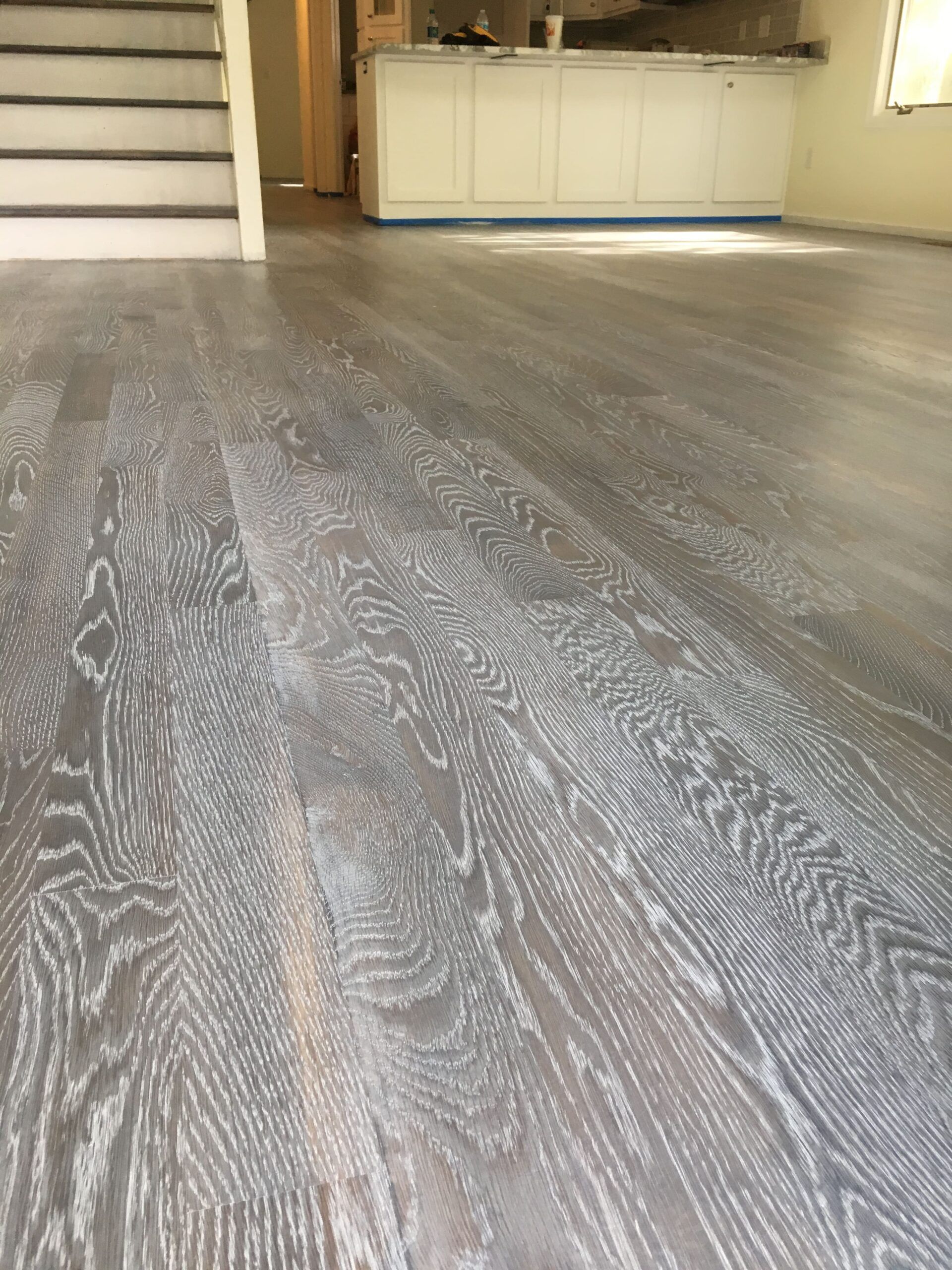 Gray wood-look floor in a room with stairs and white cabinets in the background