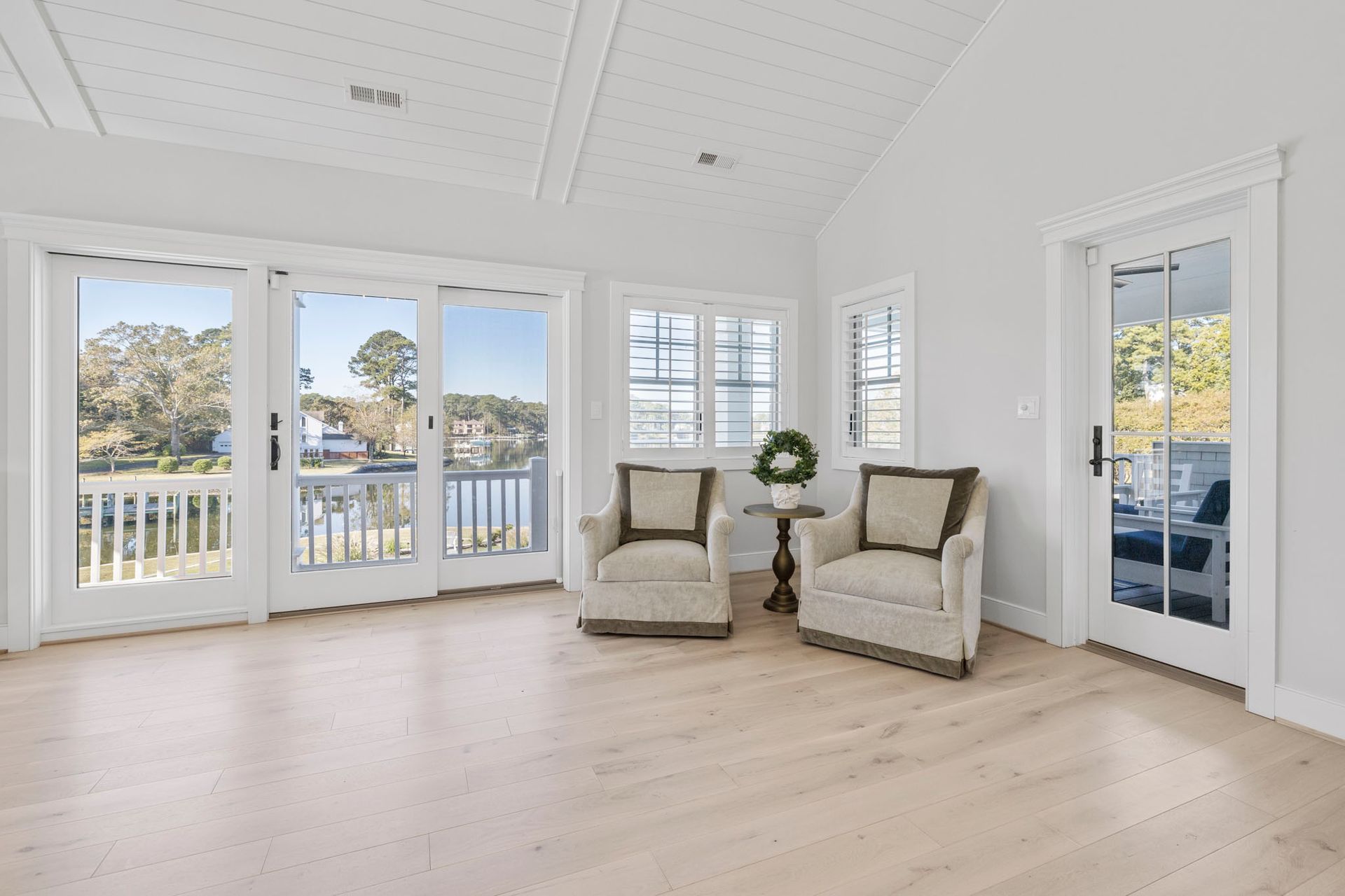 Bright white sunroom with large windows, French doors, two armchairs, and pale wood floors.