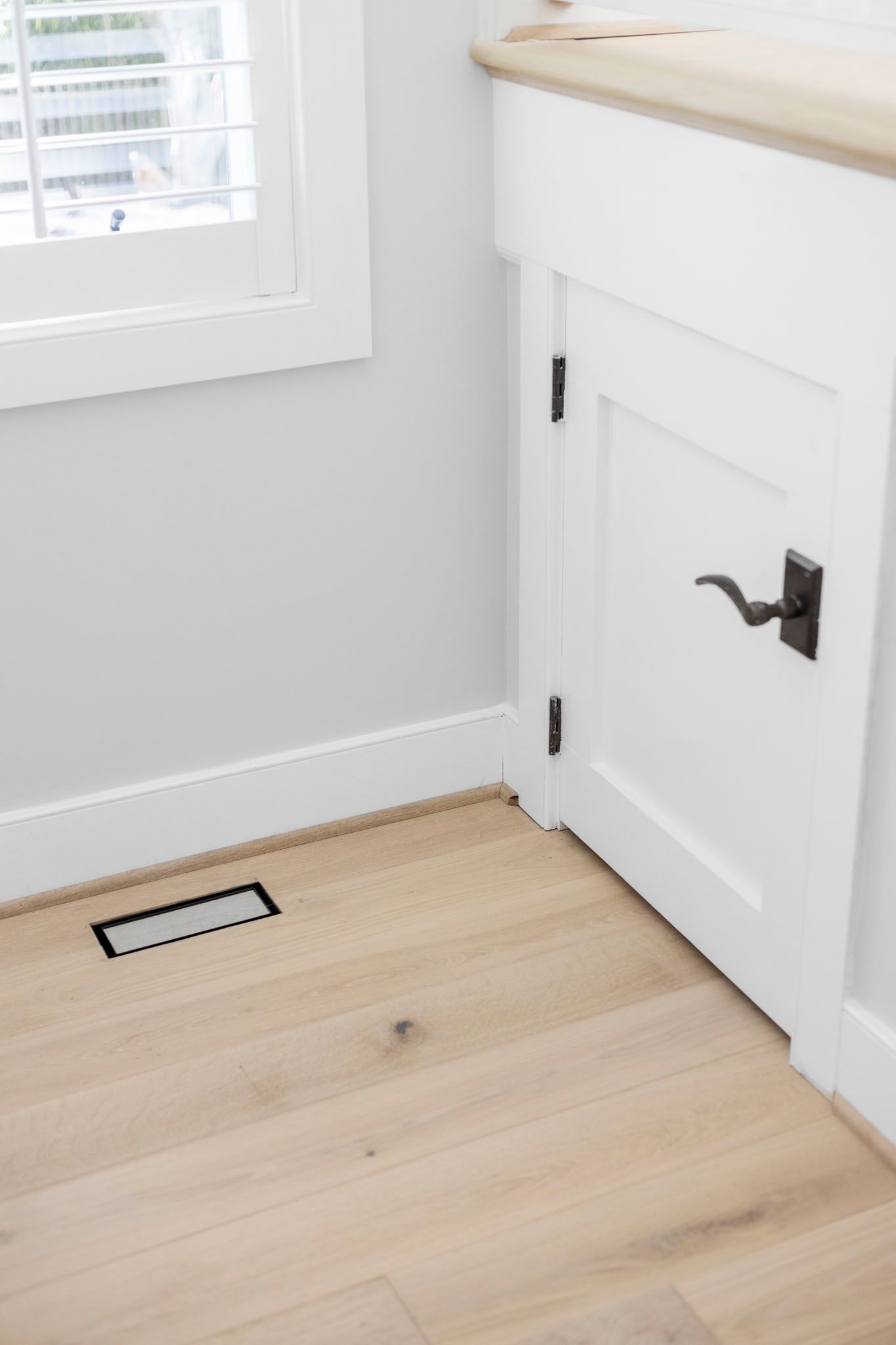 Bright white cabinet door and baseboard in a light wood-floored room near a window vent.