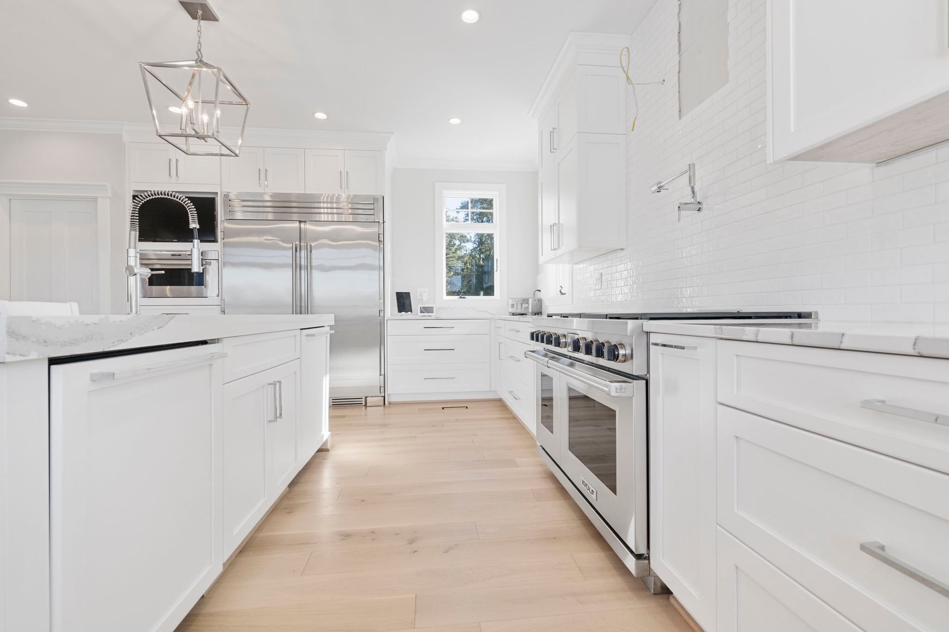 Bright modern white kitchen with light wood floors, stainless steel appliances, and island cabinets