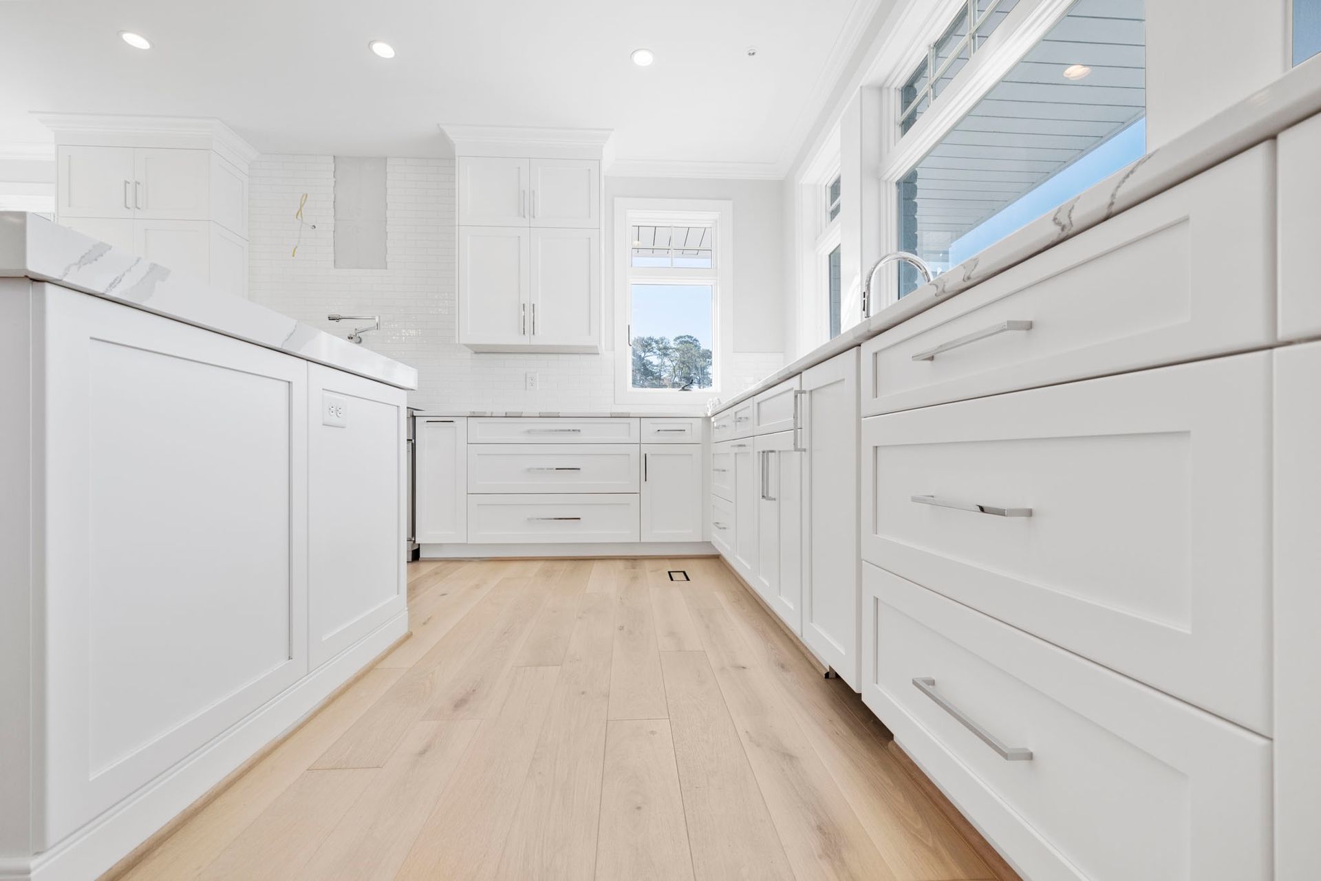 Bright white modern kitchen with pale wood floors and long countertops on both sides