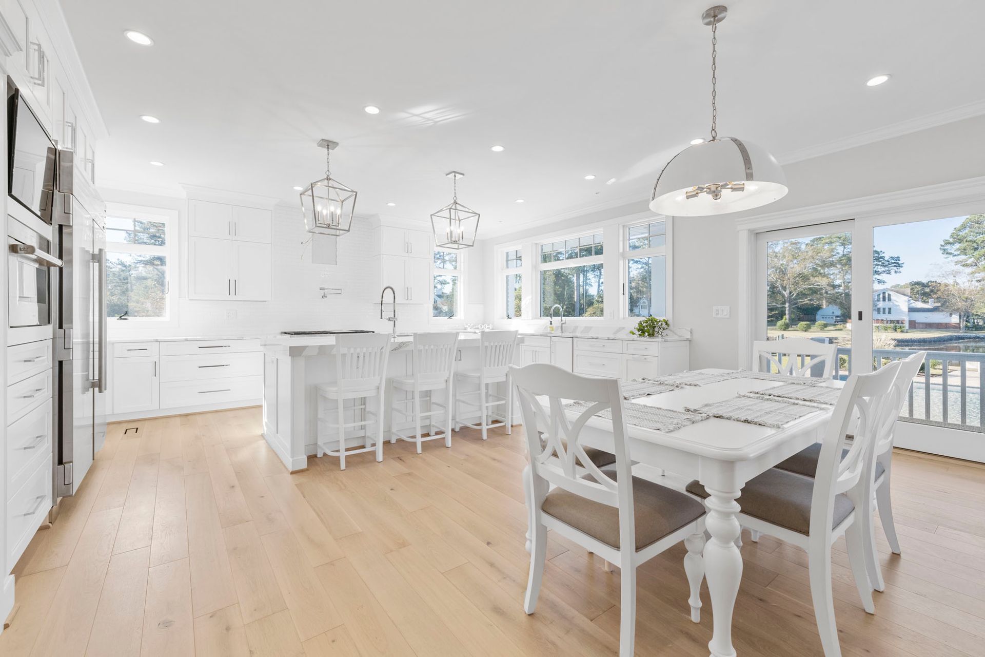 Bright white open-plan kitchen and dining room with light wood floors and large windows
