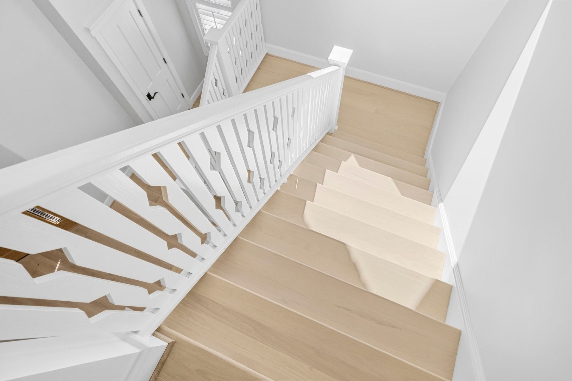 Bright staircase with light wood steps and white railing in a hallway