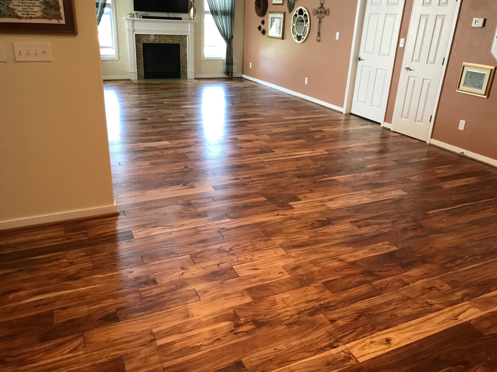 Empty living room with polished hardwood floors, tan walls, white doors, and a fireplace in the distance