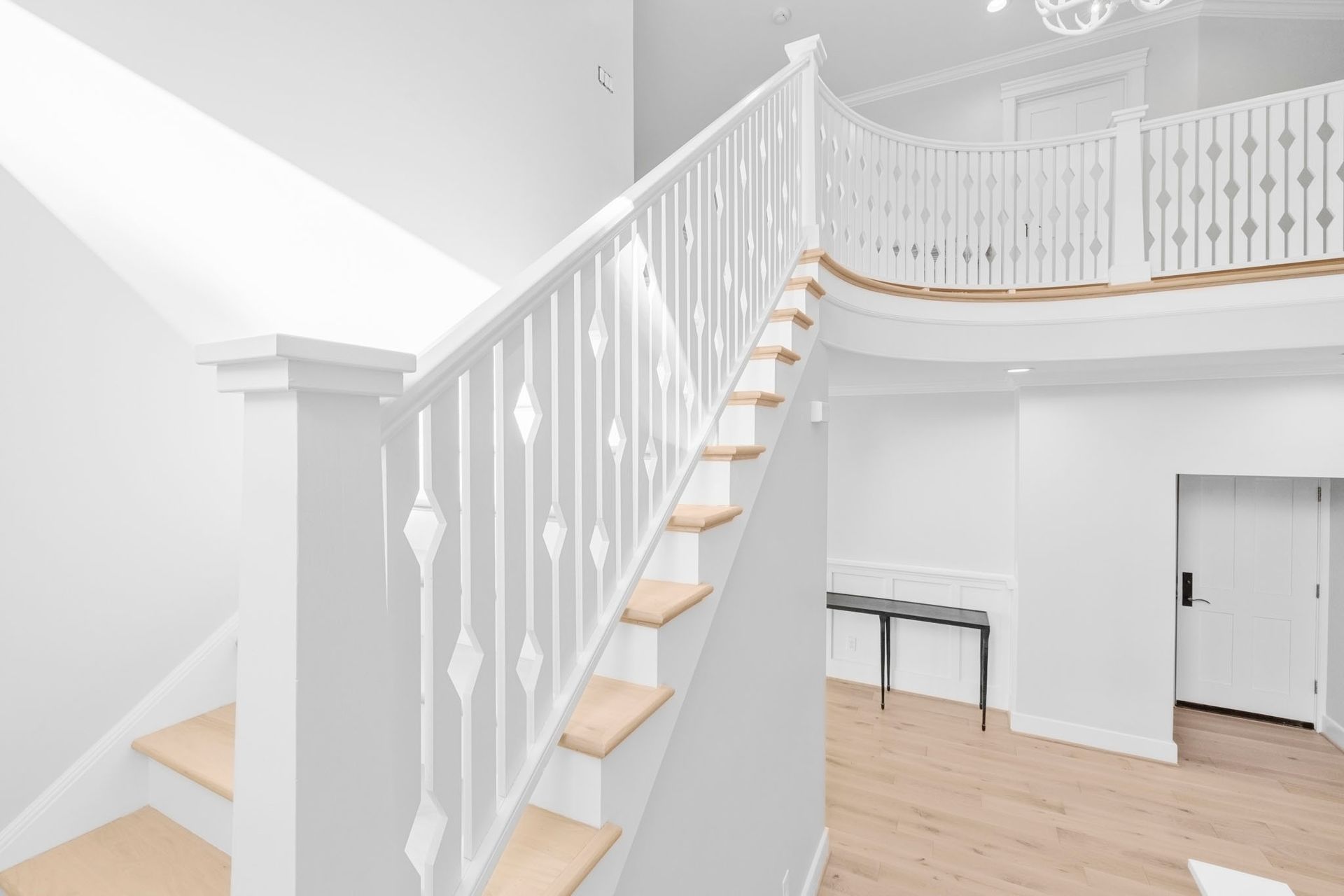 Bright white interior with a curved staircase, wood steps, balcony railing, and light hardwood floors