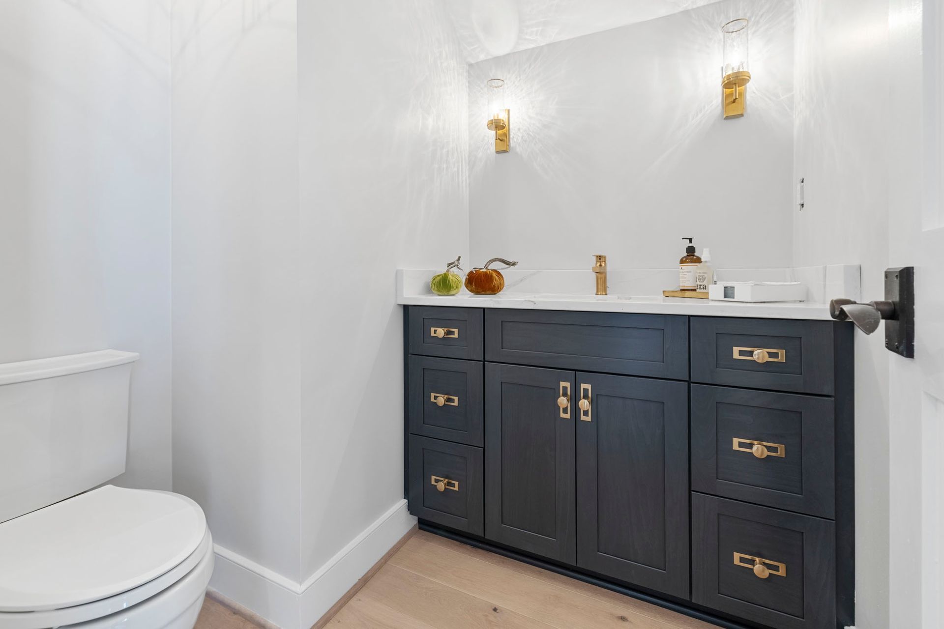 Small bathroom with dark vanity, white walls, sink, mirror, and toilet on the left.