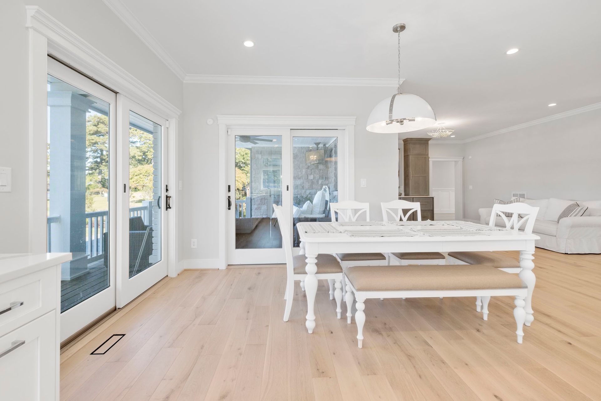 Bright white dining room with a wooden table, bench, chairs, and glass doors opening to a deck.