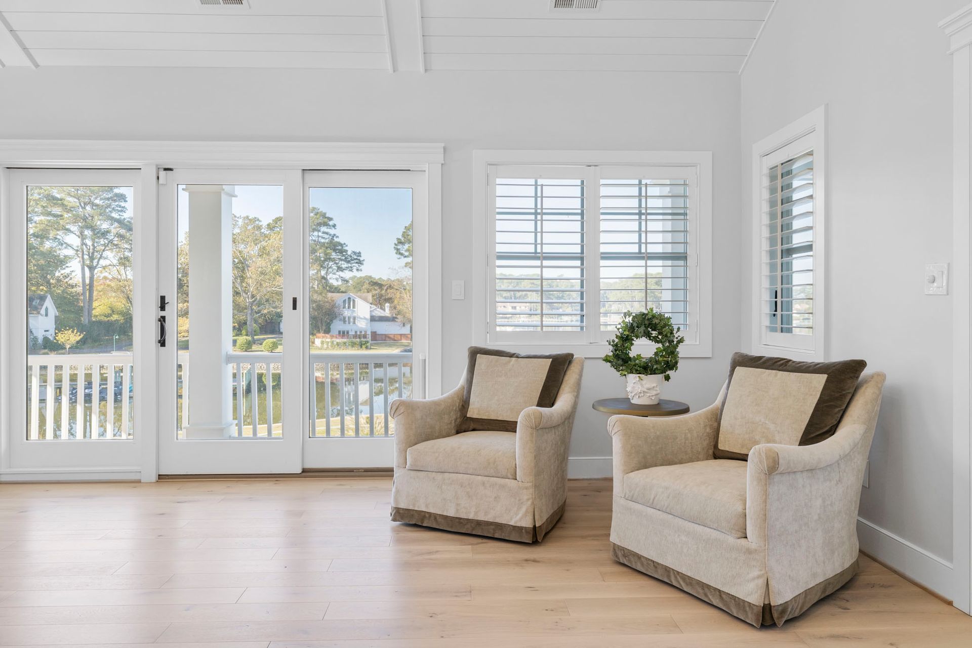 Bright living room with white walls, light wood floors, two armchairs, and large windows overlooking water.