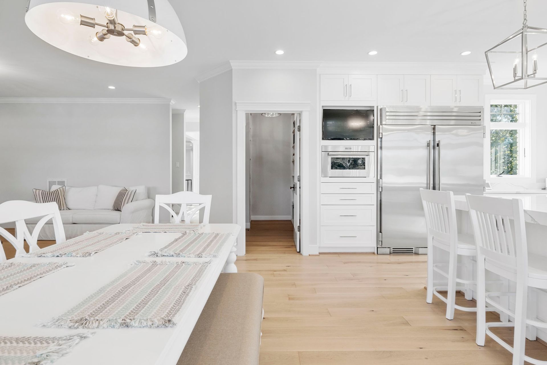 Bright white kitchen and dining area with island, stainless appliances, and light wood floors
