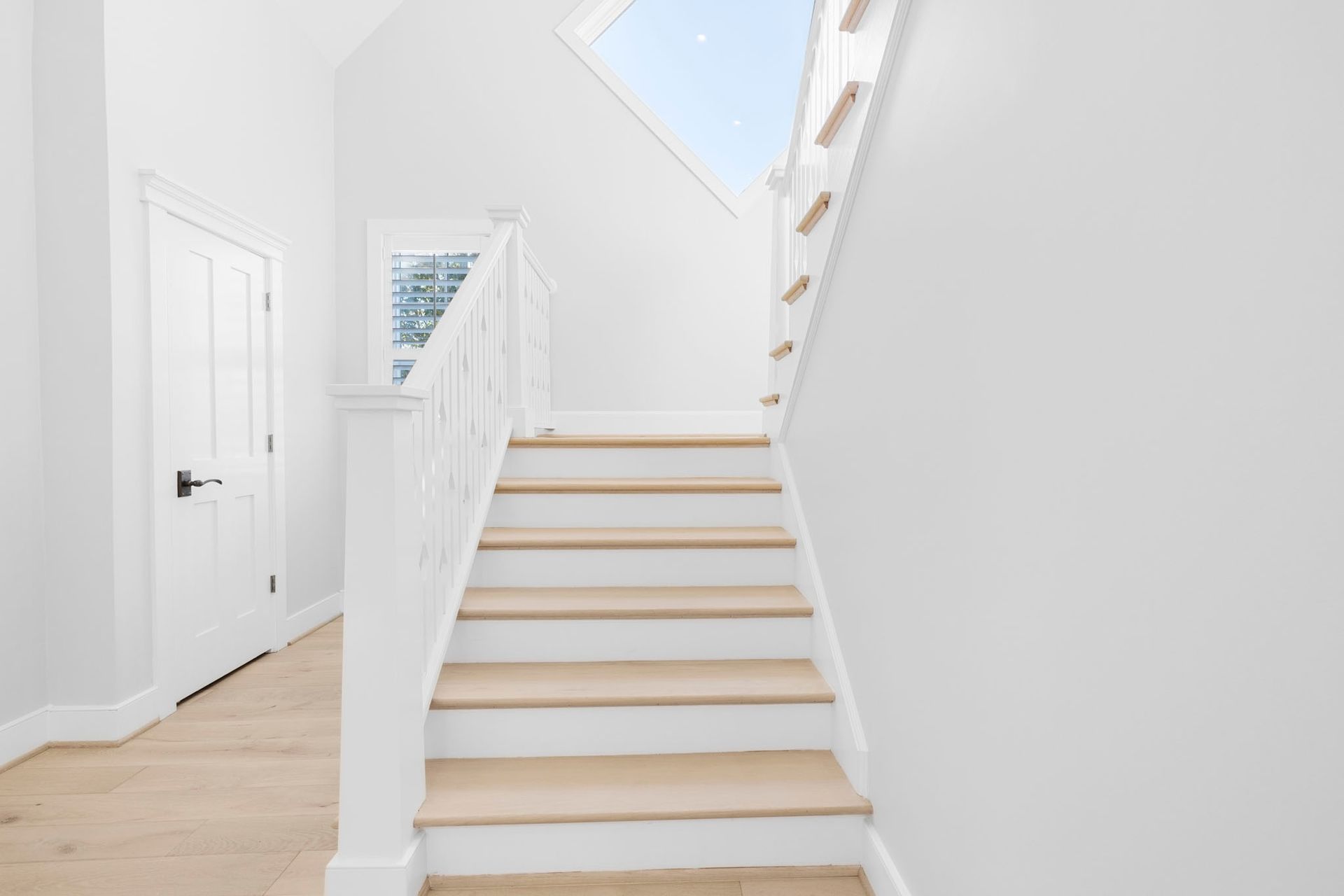Bright white staircase with wooden steps in a minimalist hallway under a skylight