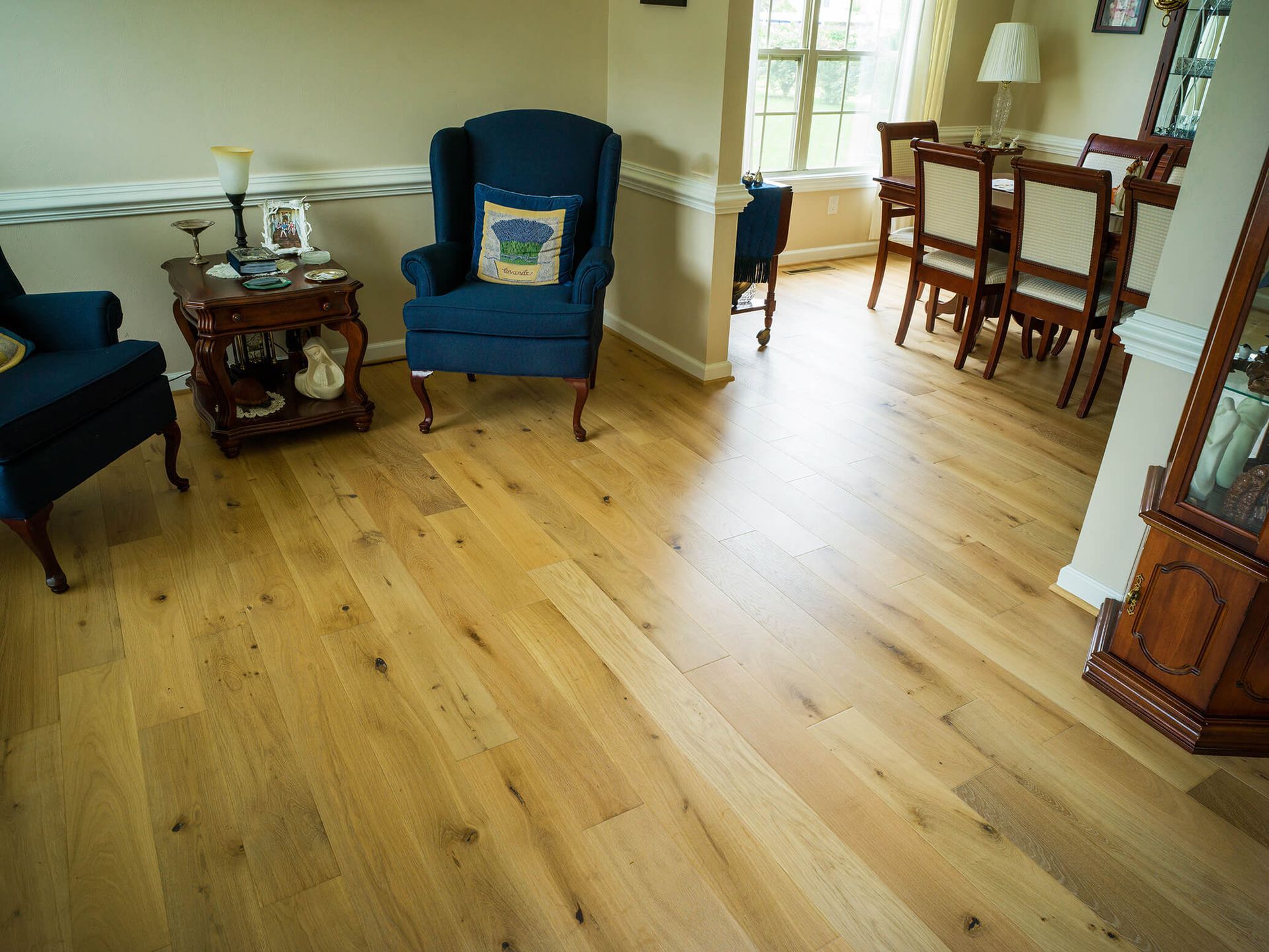 Living room with hardwood floors, blue chairs, and a dining table by a bright window