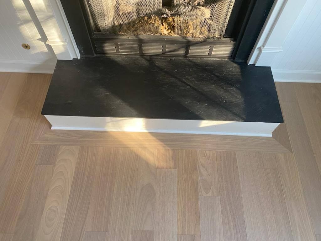 Light wood floor leading to a black fireplace hearth with white trim and firewood inside.