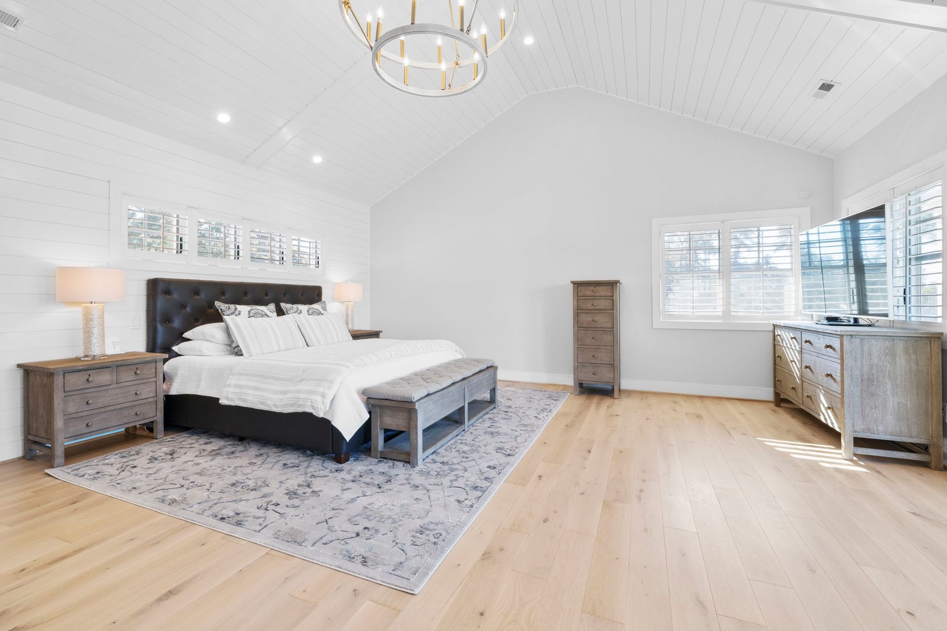 Bright bedroom with a white bed, gray rug, wood floors, and windows on two walls.