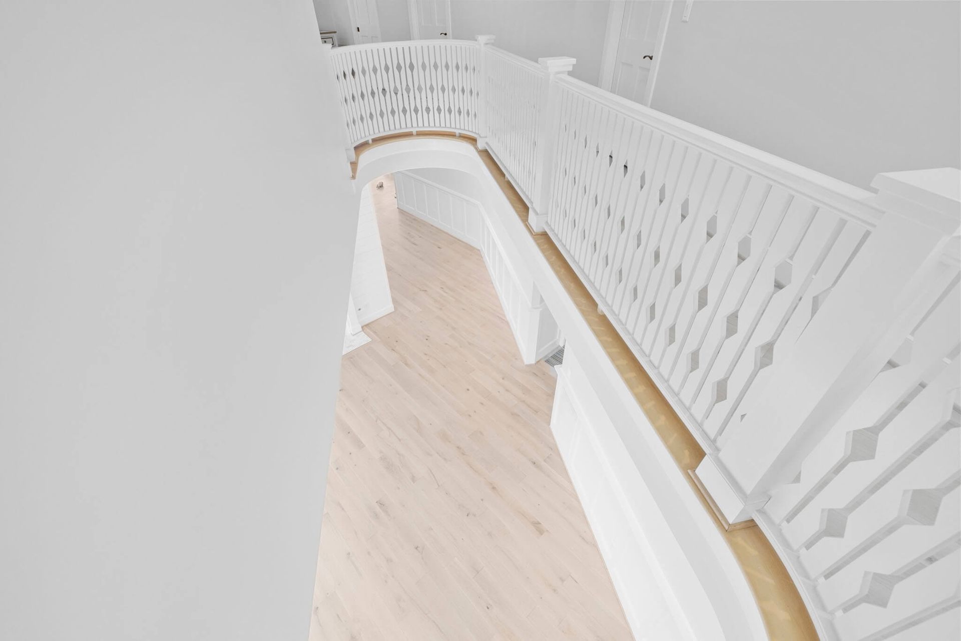 Curved white staircase with wood handrail and light wood floor in a bright interior