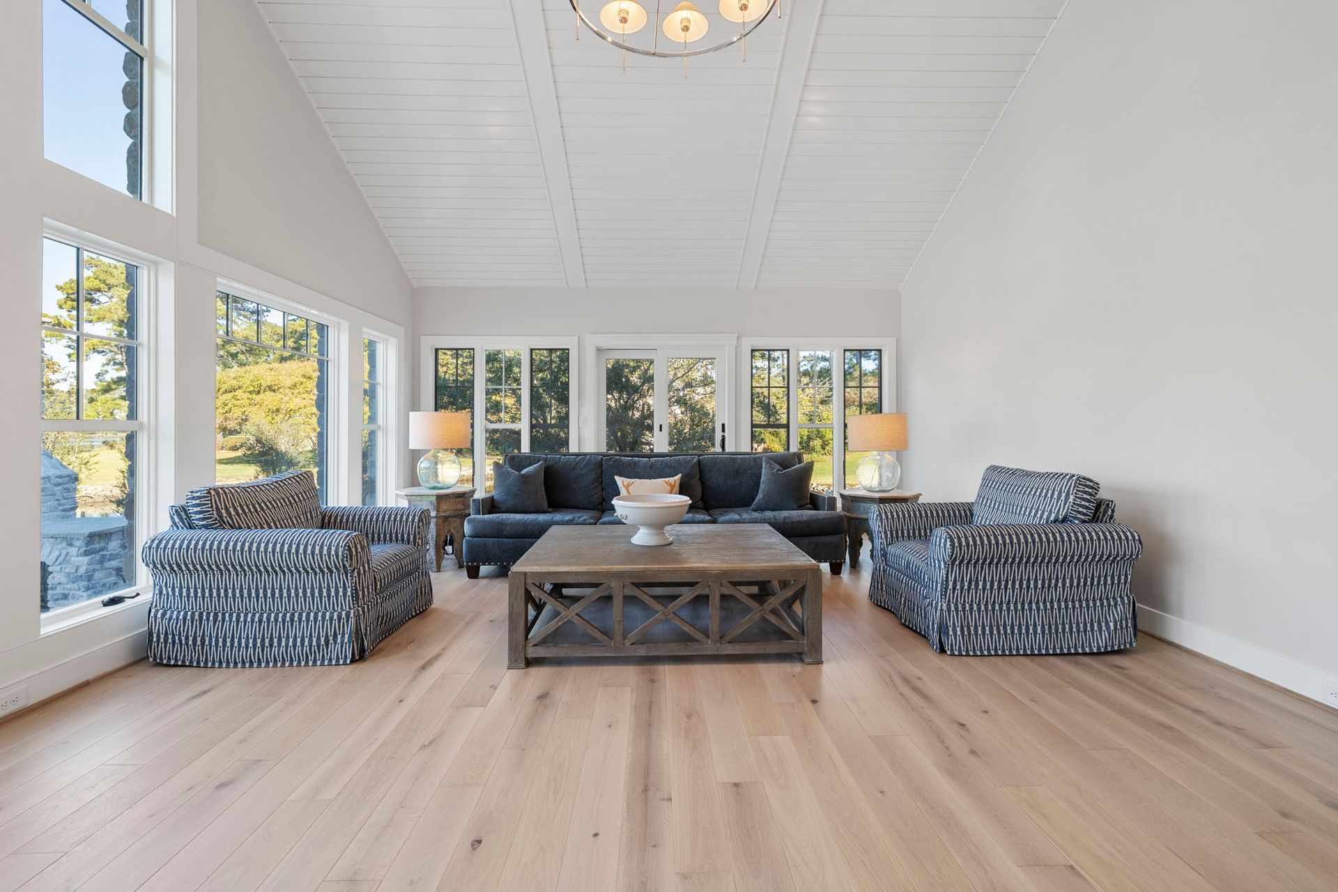 Bright living room with white walls, large windows, blue sofas, and a wooden coffee table