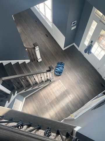 Staircase landing with gray wood floors, blue-gray walls, and a blue bag on the floor near a window.