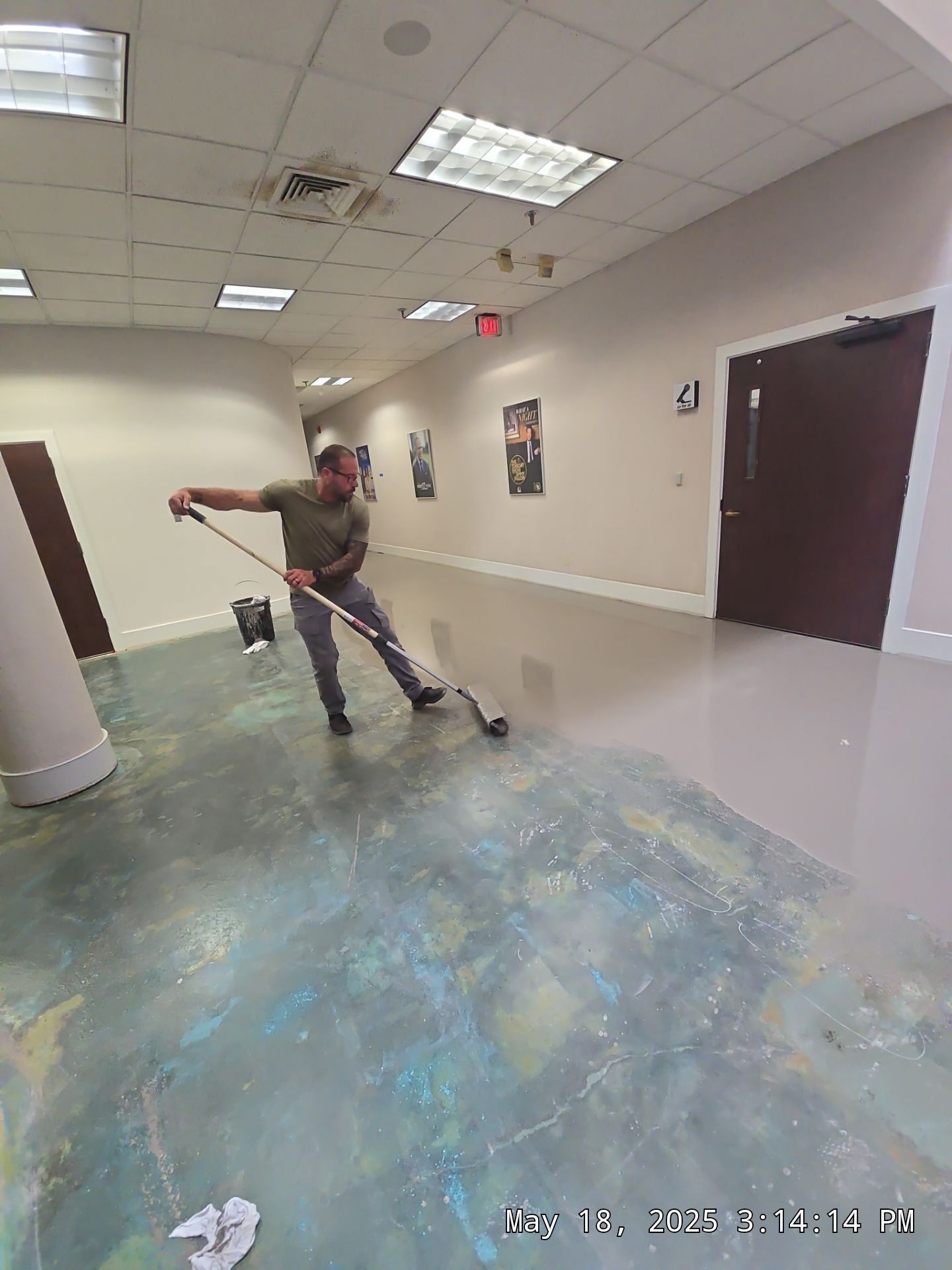 Person mops a hallway floor in a building with beige walls and fluorescent ceiling lights.