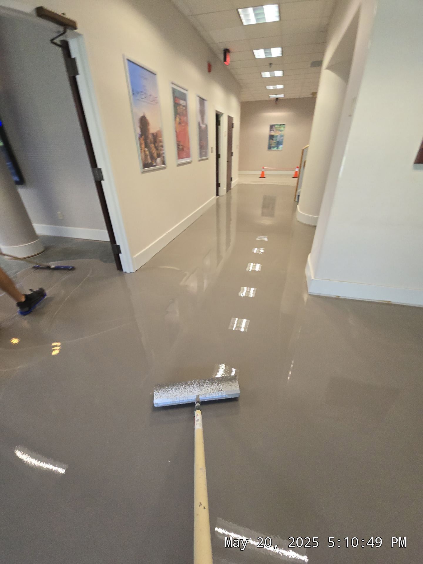Hallway with a mop on a shiny floor, poster-lined walls, and a person partially visible at left.