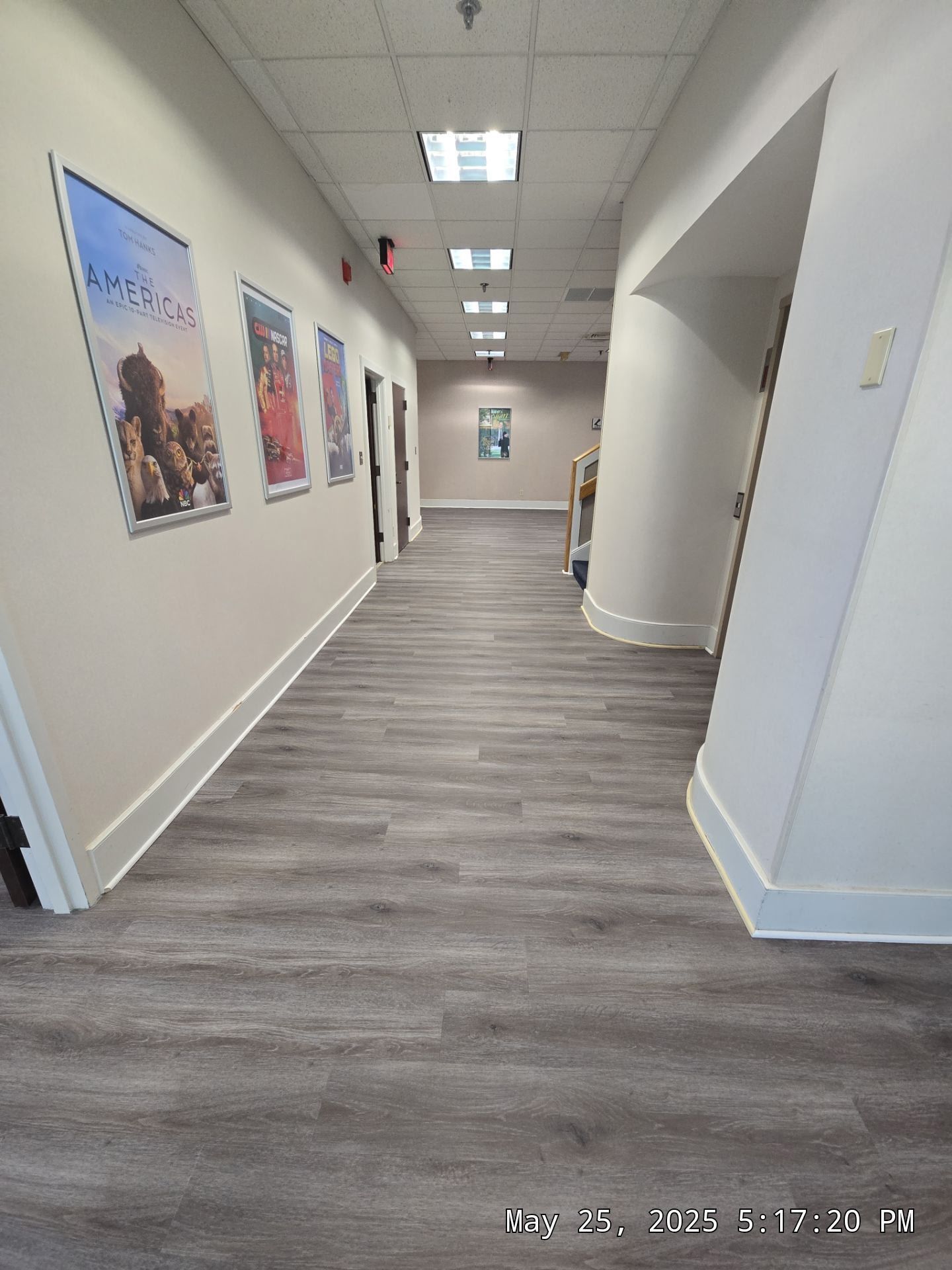 Empty office hallway with gray flooring, white walls, framed art, and bright ceiling lights.