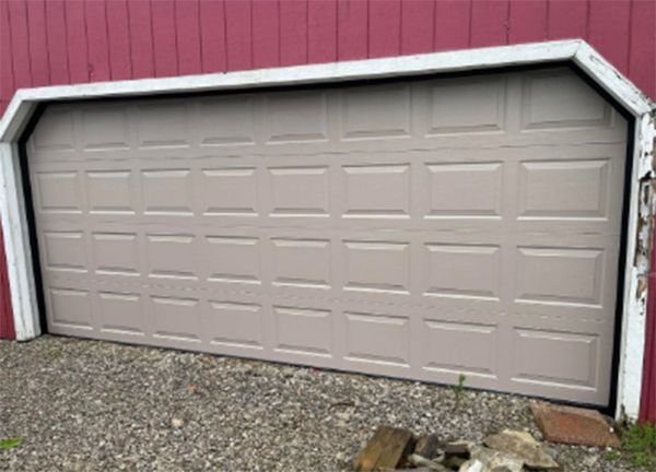 Tan garage door against a red building, surrounded by white trim and gravel.