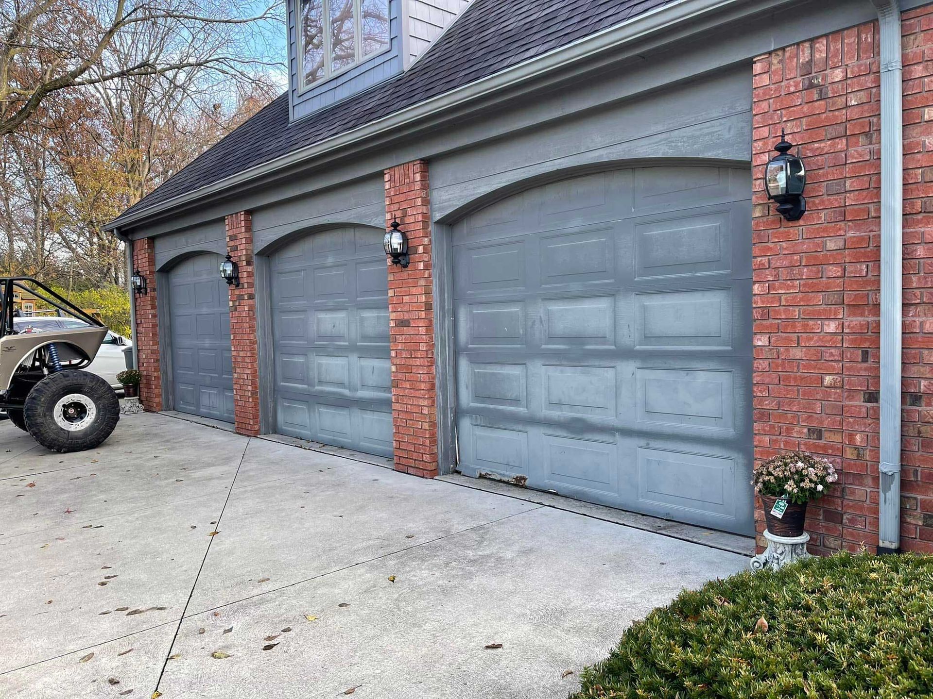 Three gray garage doors with brick accents on a house, a vehicle is parked nearby.