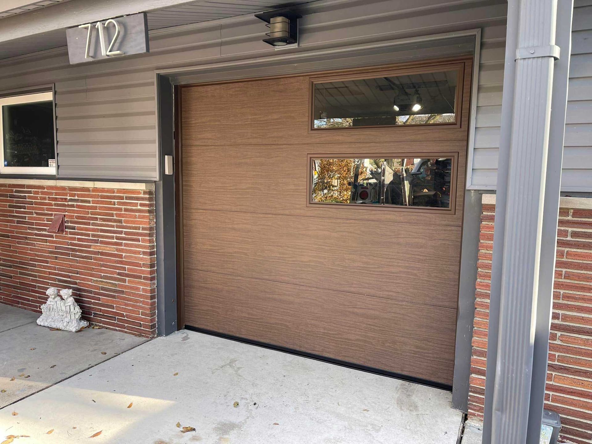 Brown garage door with two window panes, next to a brick wall and a house number.