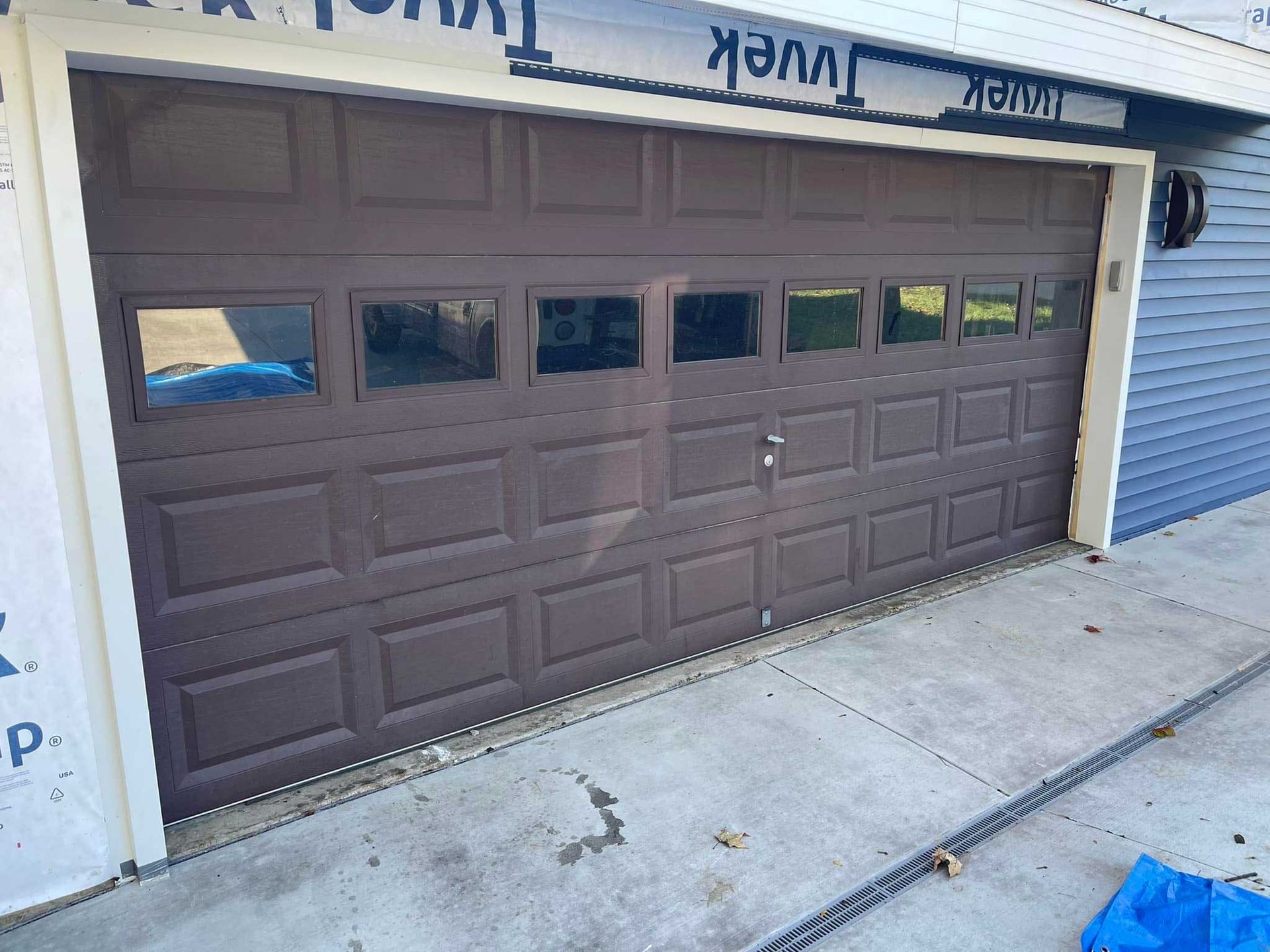Brown garage door with windows, on a house with blue siding and a concrete driveway.