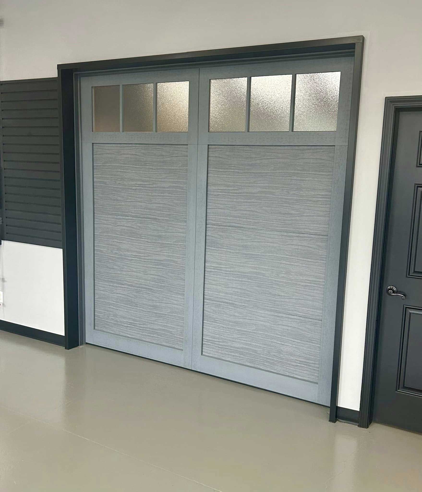 Gray garage door with textured panels and frosted glass windows.