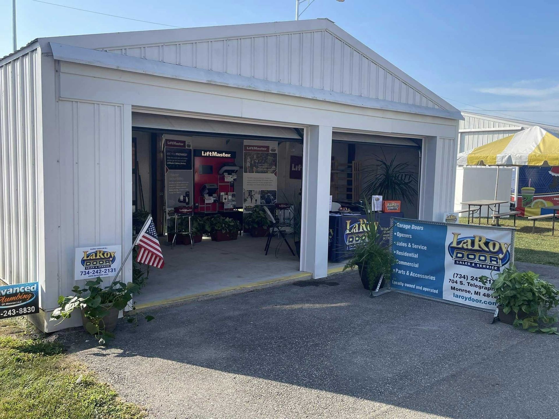 White garage with open doors, signage, and merchandise, under blue sky.