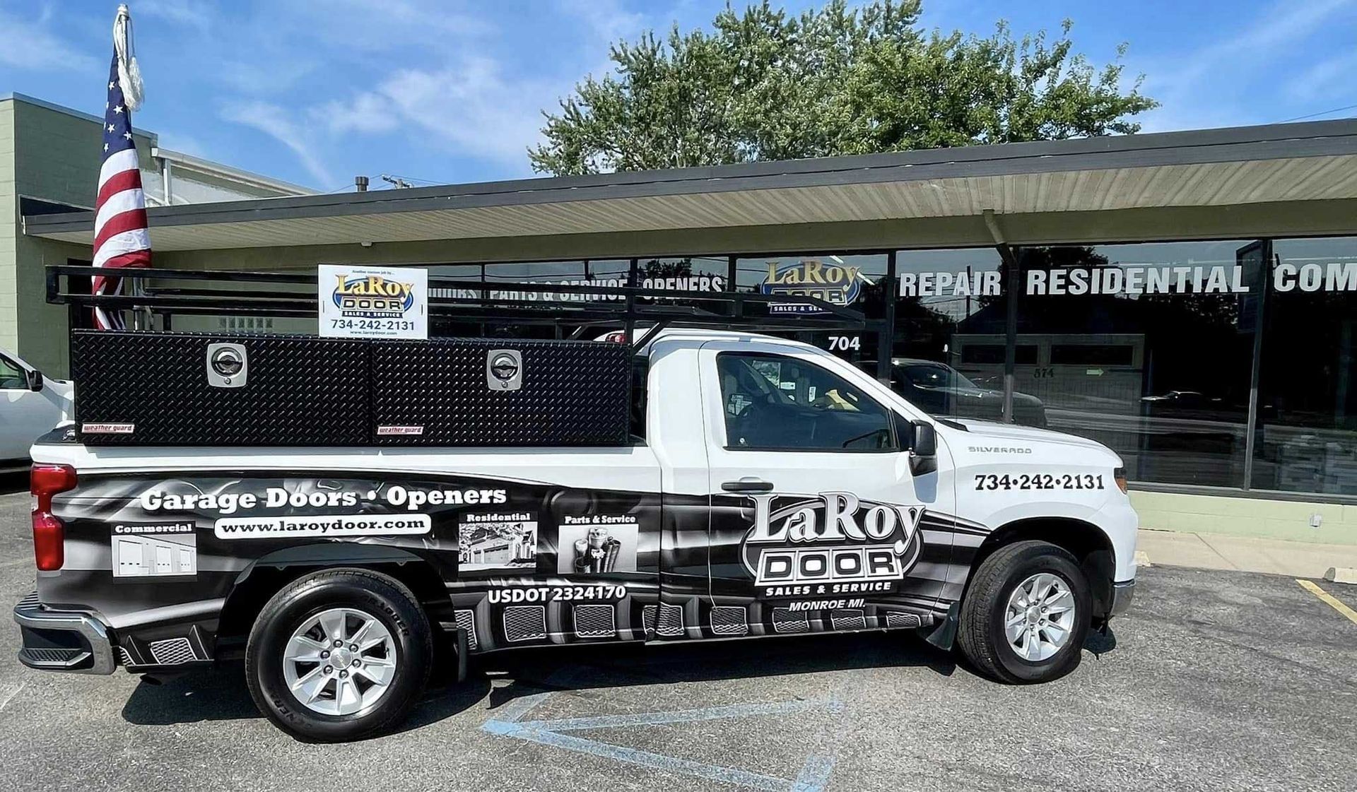 White truck with company logo parked outside a building, carrying tools and an American flag.