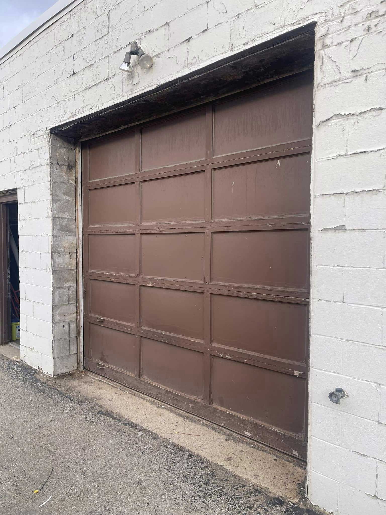 Brown garage door on a white brick building. Gray asphalt driveway.