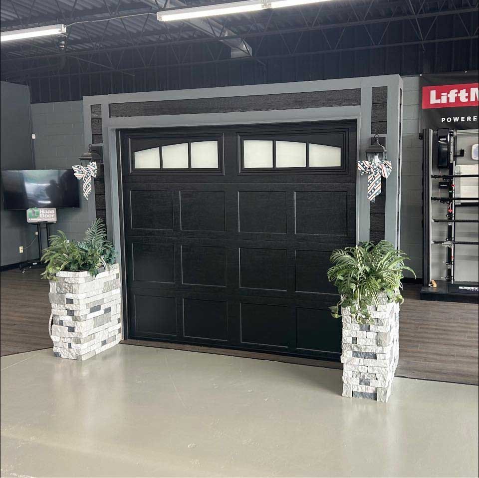 Black garage door with windows, flanked by stone planters.