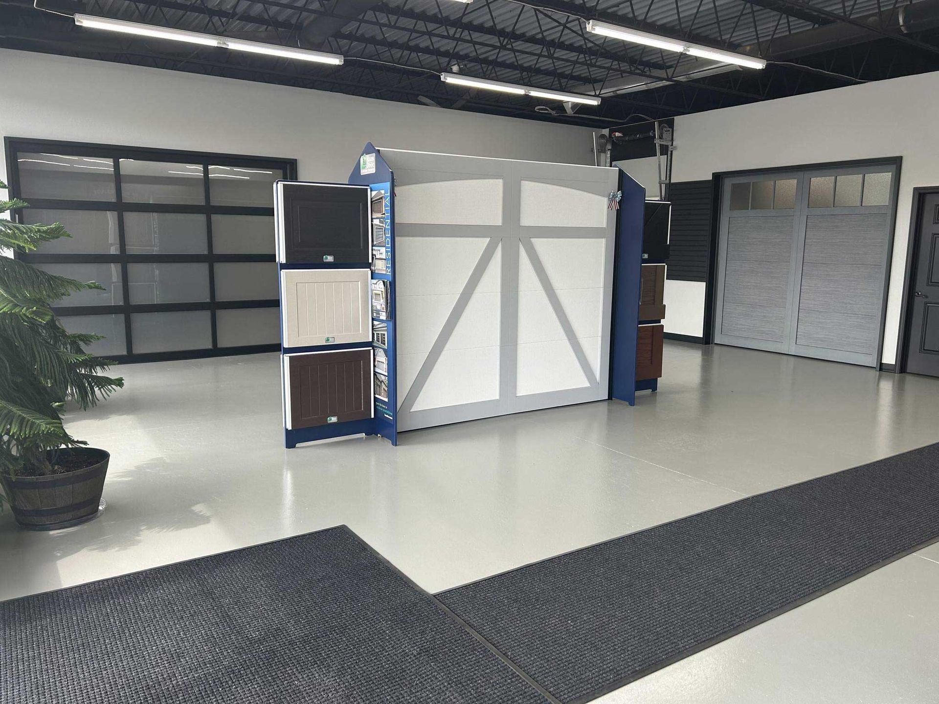 Garage door showroom with various door samples on display, including glass and wood panel designs.