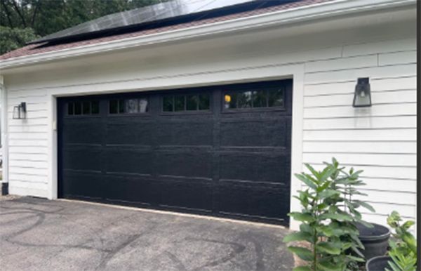 Black garage door with windows, white trim, siding, and lanterns. Solar panels on roof.
