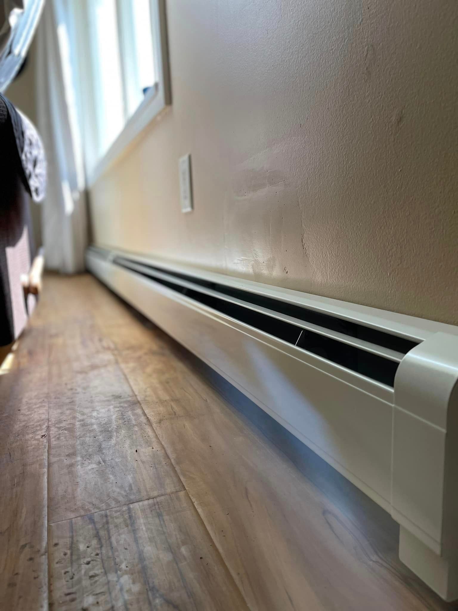 A heating system installed on a wooden floor next to a window.