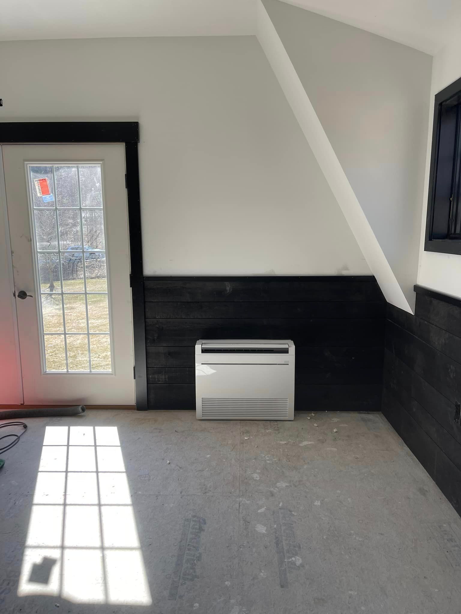 A white air conditioner is sitting in a room next to a window.