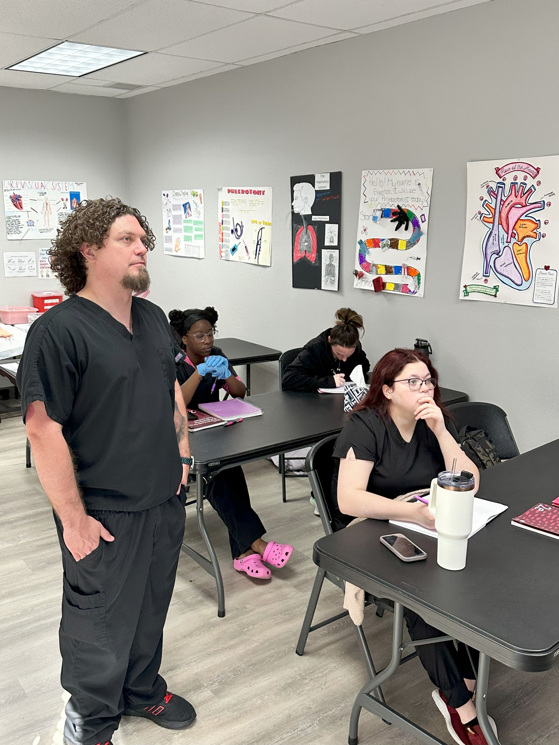 A man is standing in front of a group of people sitting at tables in a classroom.