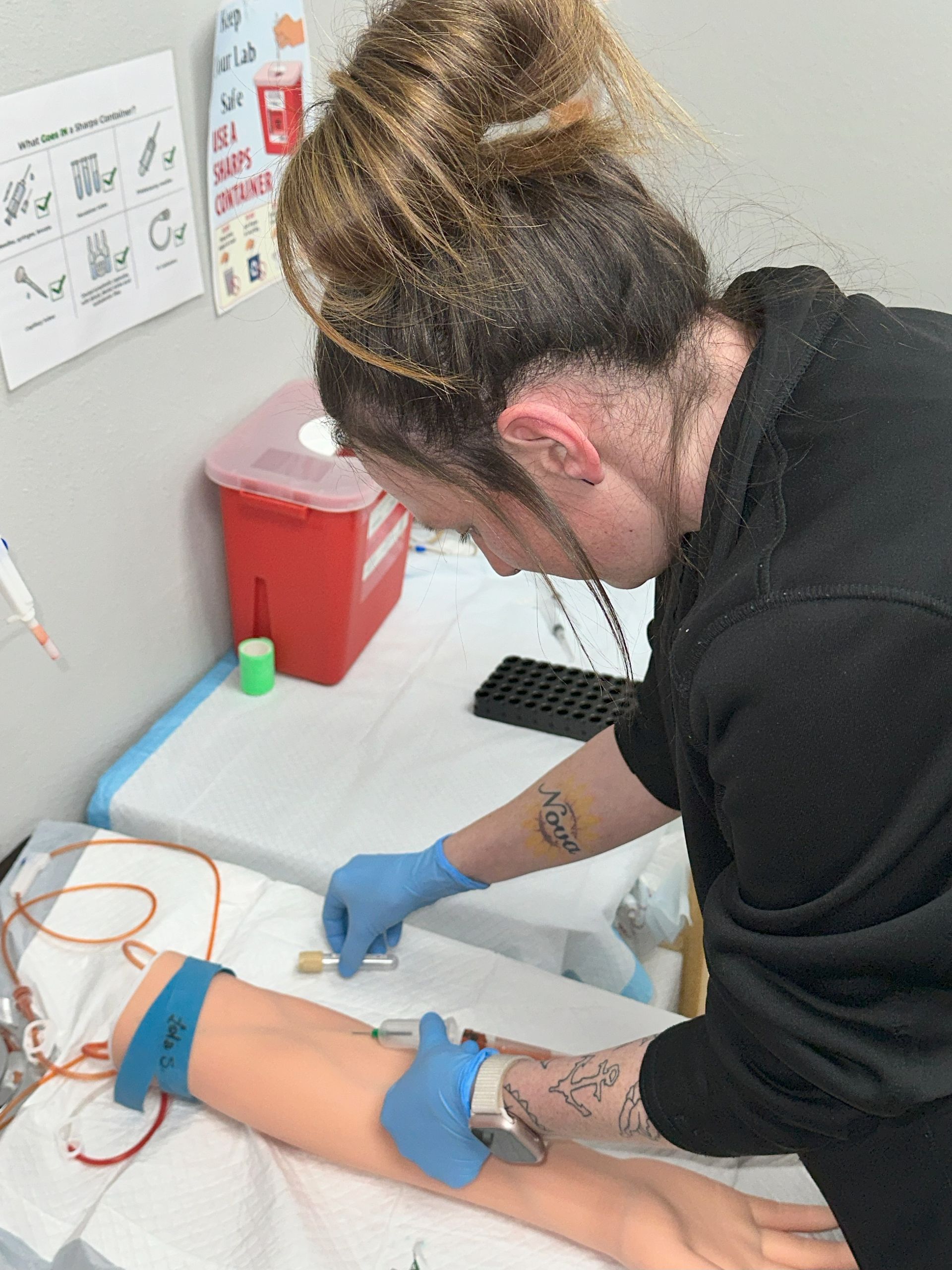 A nurse practicing on a simulated patient's arm in a classroom.
