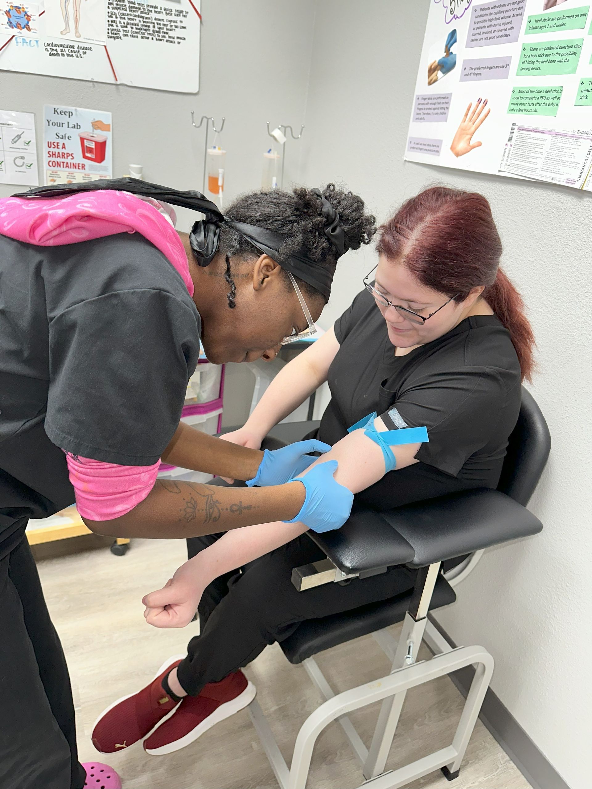 Two nurses are working on a patient's arm in a classroom.