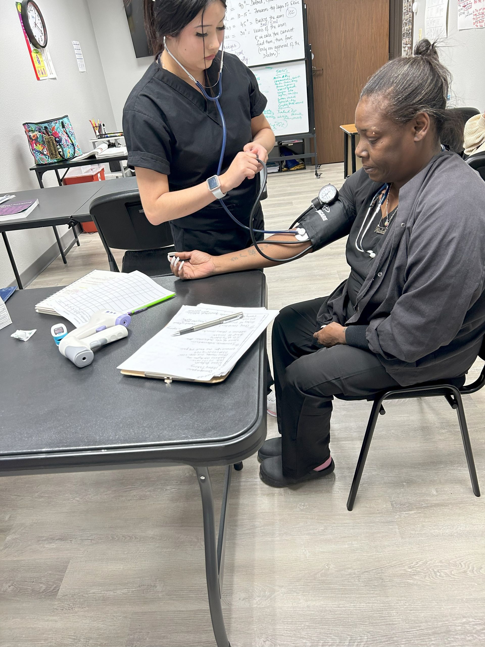 Two nurses are working on a patient's arm in a classroom.